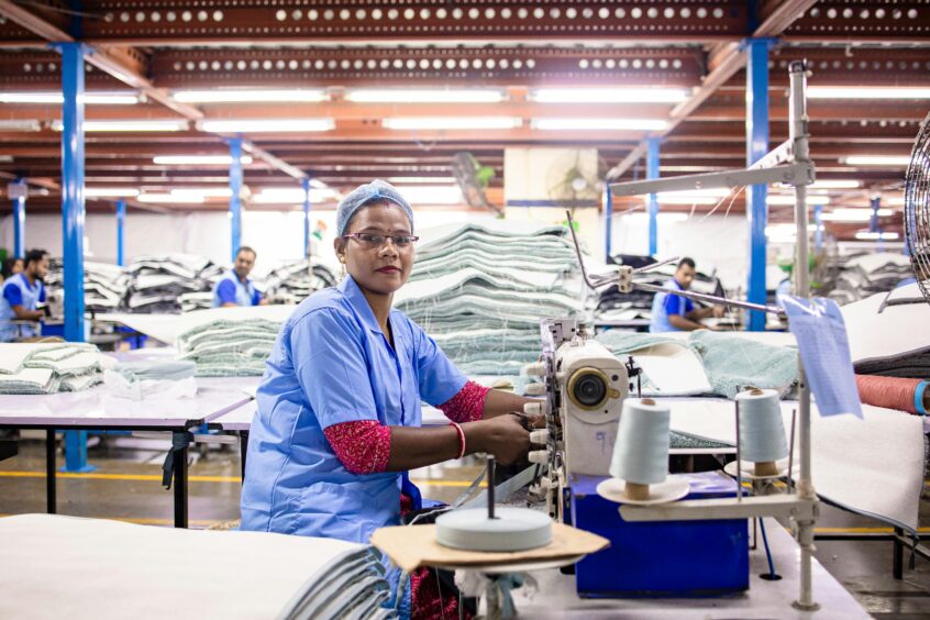 Female worker sewing textiles in a bustling factory environment, showcasing industrial labor.