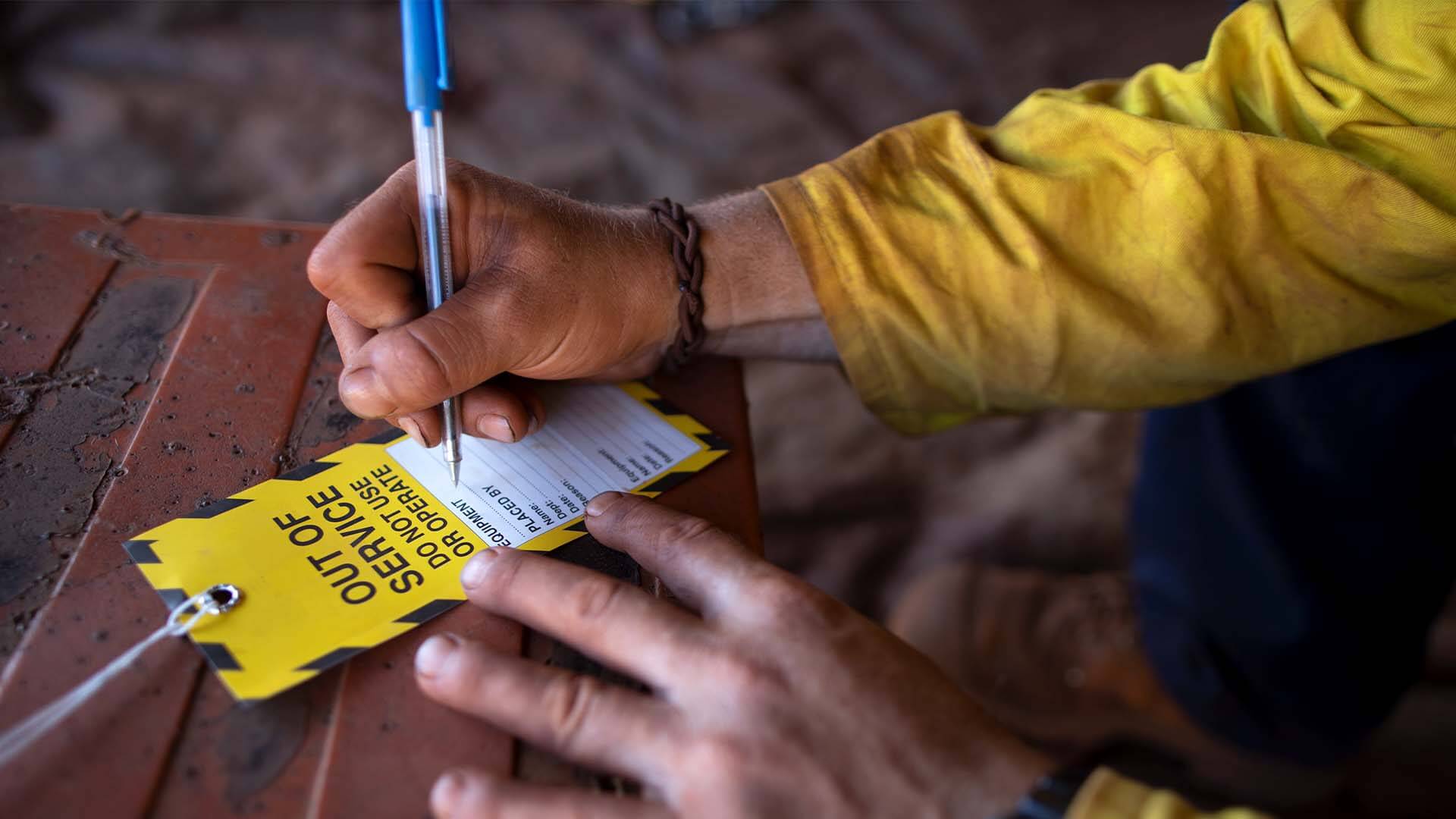 Up close photo of a construction or factory worker placing a note on a defective or dangerous product like a power tool to let people know not use it
