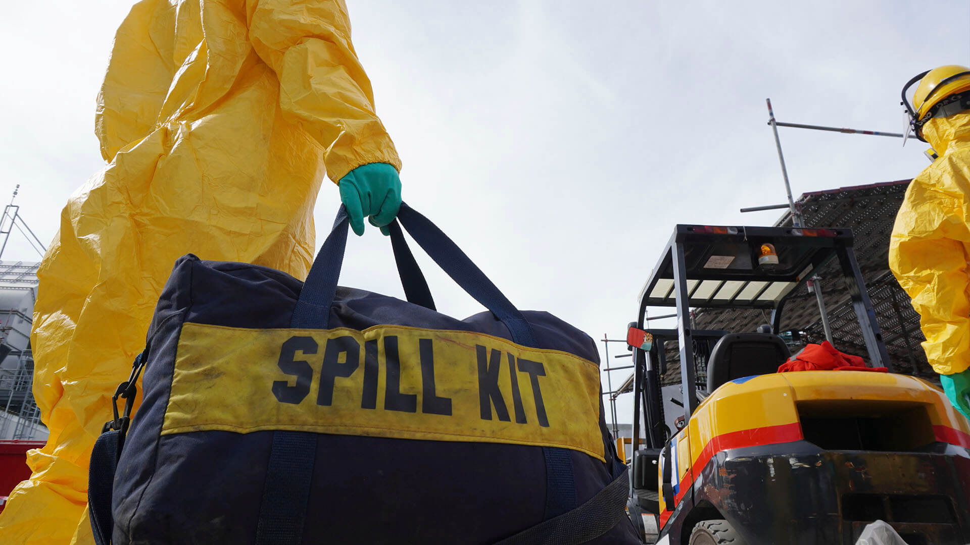 Worker in a hazmat suit carrying spill kit to a chemical burn accident