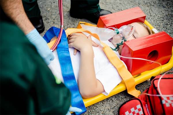 A young child laying on a stretcher after suffering a person injury - he is aided by paramedics who have placed a neck brace and breathing mask on him